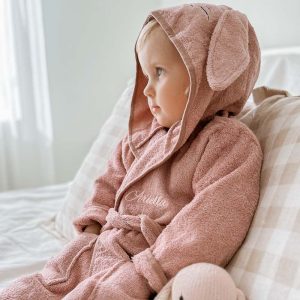 A toddler wearing a blush pink bunny robe that is personalised with embroidery.