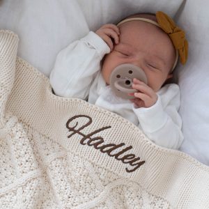 A baby under a cream diamond baby blanket personalised with the name Hadley/