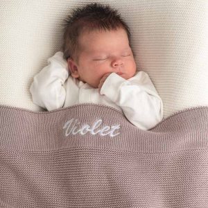 Baby sleeping under personalised dusty lilac knitted cotton newborn blanket embroidered with the girls name Violet.