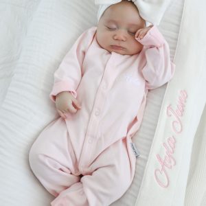 Baby wearing pink onesie with personalised white knitted blankets newborn present.