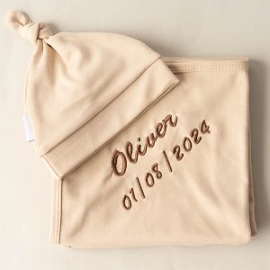 A beige beanie and swaddle embroidered with brown thread.