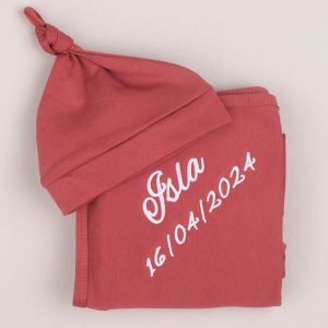 A burgandy coloured beanie and swaddle embroidered with the name Isla.