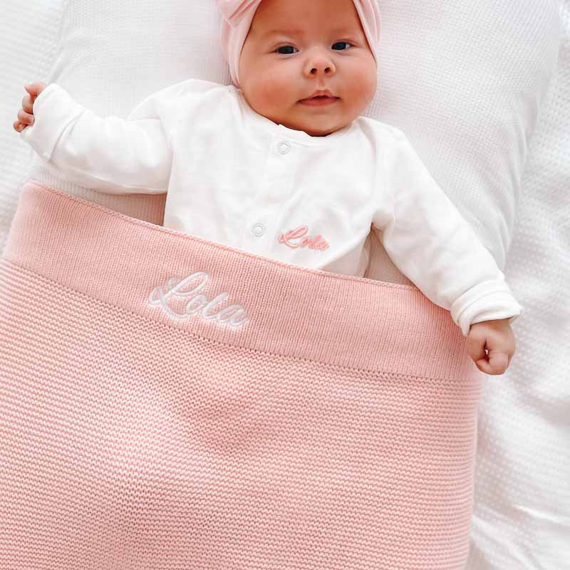 Baby girl wearing personalised white onesie with pink knitted blanket newborn girl gift.