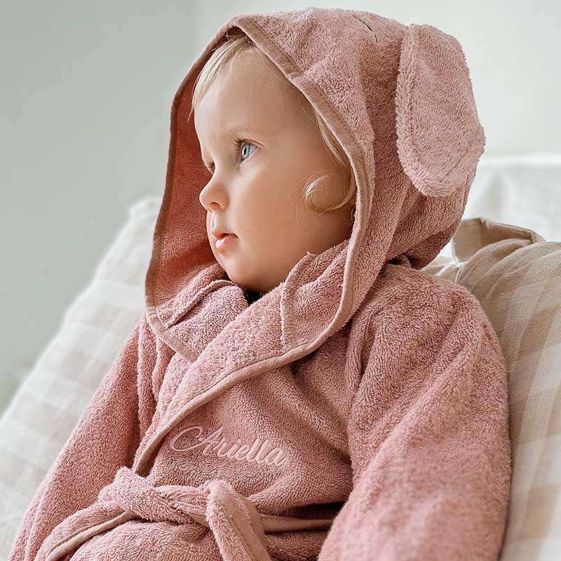 Girl wearing personalised pink hooded baby bathrobe 1 year old gift.