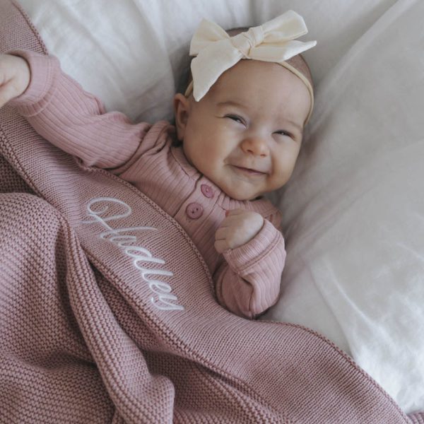 Hadley wearing a romper and head band under a blush pink blanket personalised baby girl gift.