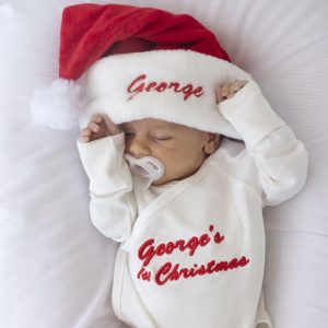 A Personalised Baby Christmas Hat and Romper Gift Set embroidered with red text.