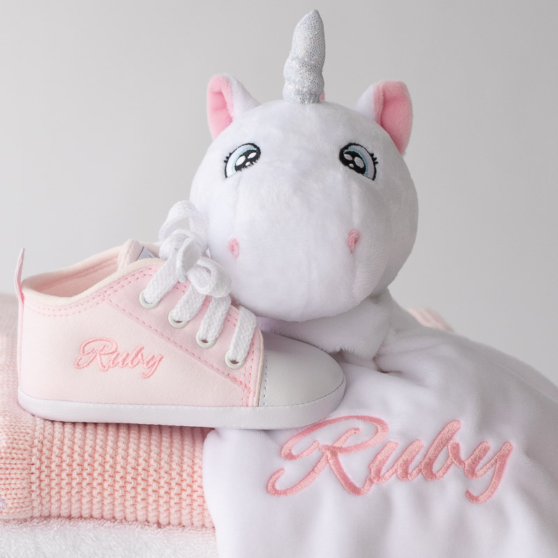 A pink baby shoe and unicorn baby comforter both personalised with the name Ruby.