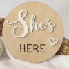 A birth wood birth announcement disc that says "She's Here" with a heart in white acrylic overlayed.